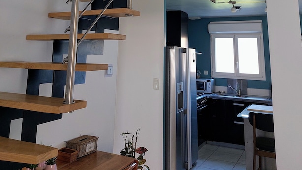 Eine moderne Küche mit Einbaukühlschrank, ein Essbereich mit Holztisch und -stühlen sowie eine Treppe mit Holzstufen und Metallgeländern.