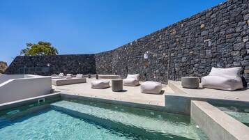 A pool area with stone walls, lounge chairs, and a clear blue pool.