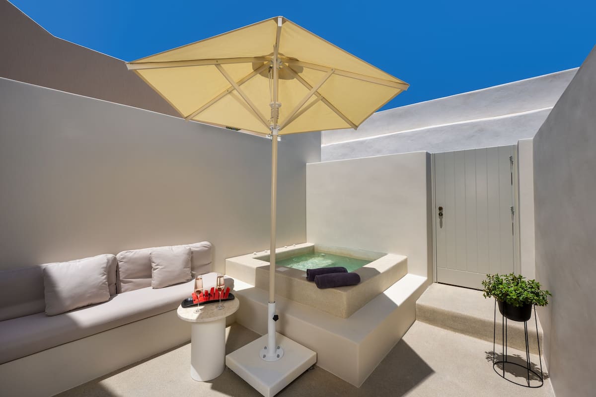 Un espacio moderno al aire libre para relajarse, con un sofá beige, una mesita con una copa y un jacuzzi.
