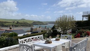 A table set outdoors with white chairs, overlooking a coastal landscape with boats and hills. - Unique period house in the heart of Salcombe (Salcombe)