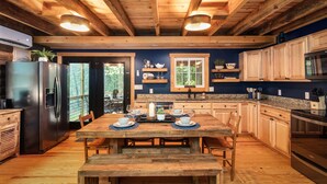 Una cocina rústica con vigas de madera, una gran mesa de comedor preparada para cuatro personas y electrodomésticos modernos.