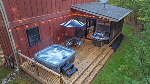 Ett bubbelbad, en utomhusgrill och trädgårdsmöbler på ett trädäck, dekorerat med ljusslingor.
