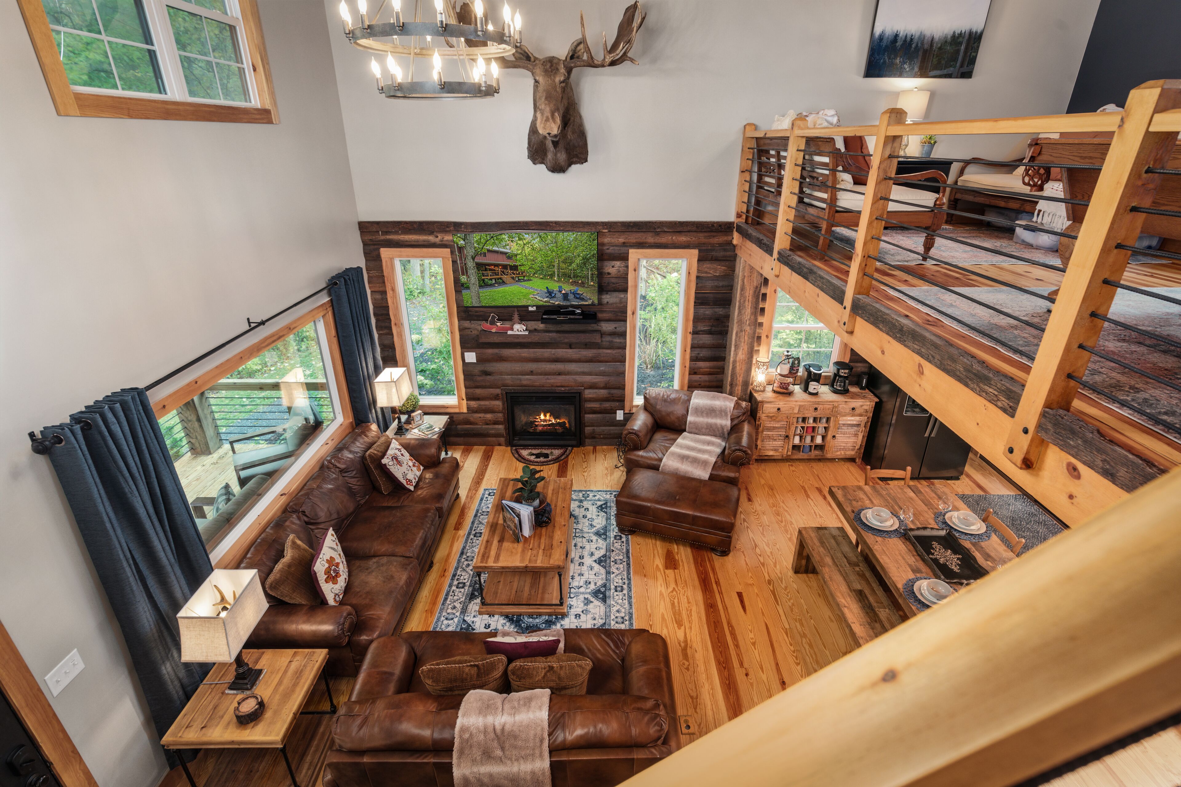 Un intérieur de chalet chaleureux avec une cheminée, des canapés en cuir, des meubles en bois et une grande fenêtre donnant sur une forêt.