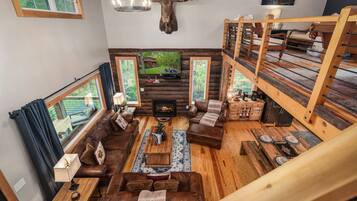 Un intérieur de chalet chaleureux avec une cheminée, des canapés en cuir, des meubles en bois et une grande fenêtre donnant sur une forêt.