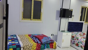 Een slaapkamer met een bed, een televisie, een dressoir en een raam met hor.