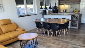 A modern living room with a sofa, a dining table with chairs, and a kitchen area with a sink and appliances.