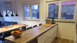 A modern kitchen with a wooden island, a dining area with a table and chairs, and a view of the outside through large windows.