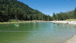 Un llac amb persones nedant i banyant-se, envoltat d'arbres i turons.