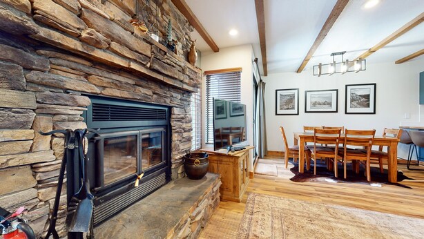 A stone fireplace with a TV, wooden dining table, and chairs in a cozy room. - Pet-Friendly, Updated Décor. Washer/Dryer, Balcony, Short Walk to The Village (Mammoth Lakes)