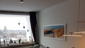 Ein modernes Wohnzimmer mit einer Couch, einem Holzes Esstisch und Blick auf eine verschneite Landschaft durch das Fenster.