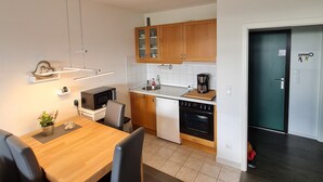 Eine kompakte Küche mit Holzschränken, einer Mikrowelle, einer Kaffeemaschine und einem Essbereich mit Tisch und Stühlen.