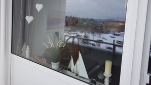 Ein Fenster mit Blick auf eine verschneite Landschaft, ein Blumentopf und eine Kerze im Fensterbrett.