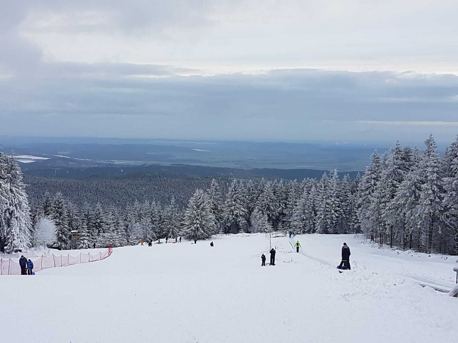 A snowy ski slope with a view of a forested area and distant landscapes.