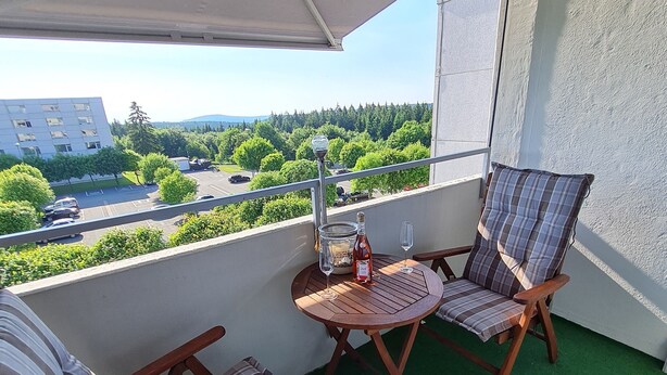 Ein Balkon mit zwei Holzstühlen, einem kleinen runden Tisch und einer Weinflasche.
