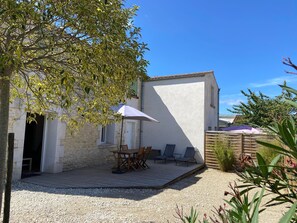 A patio with a table and chairs, a white building, and a tree.