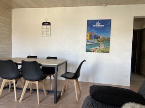 A dining area with a wooden table and black chairs, a wine rack, and a poster of a coastal scene.