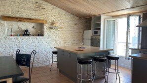 A kitchen with a stone wall, wooden ceiling, and a bar area with stools. - OCEAN, La Maison Nakety, 3 mins from Château d'Oléron beach (Le Château-d'Oléron)