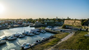 A marina with boats docked, a road, and a hill with a fort-like structure in the background. - OCEAN, La Maison Nakety, 3 mins from Château d'Oléron beach (Le Château-d'Oléron)