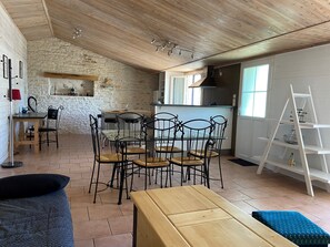 A cozy, rustic interior with a stone wall, wooden ceiling, and a dining area with metal chairs and a glass table.