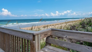 A wooden deck overlooking a beach with waves and dunes.