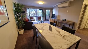 A modern living room with a marble dining table, a sofa set, a coffee table, and a potted plant. - 1BR Executive Apartment, in City Centre (Braddon)