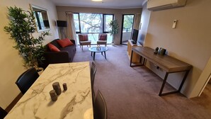 A modern living room with a marble coffee table, a sofa with red cushions, and a dining area with a wooden table and chairs. - 1BR Executive Apartment, in City Centre (Braddon)