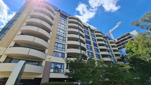 A multi-story building with balconies, a construction crane in the background, and a clear sky. - 1BR Executive Apartment, in City Centre (Braddon)