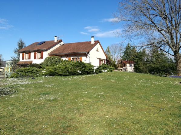 Una casa con techo inclinado, chimenea y jardín con flores blancas.