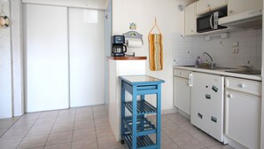 Una cocina compacta con armarios blancos, un carrito azul, un microondas y una cafetera.