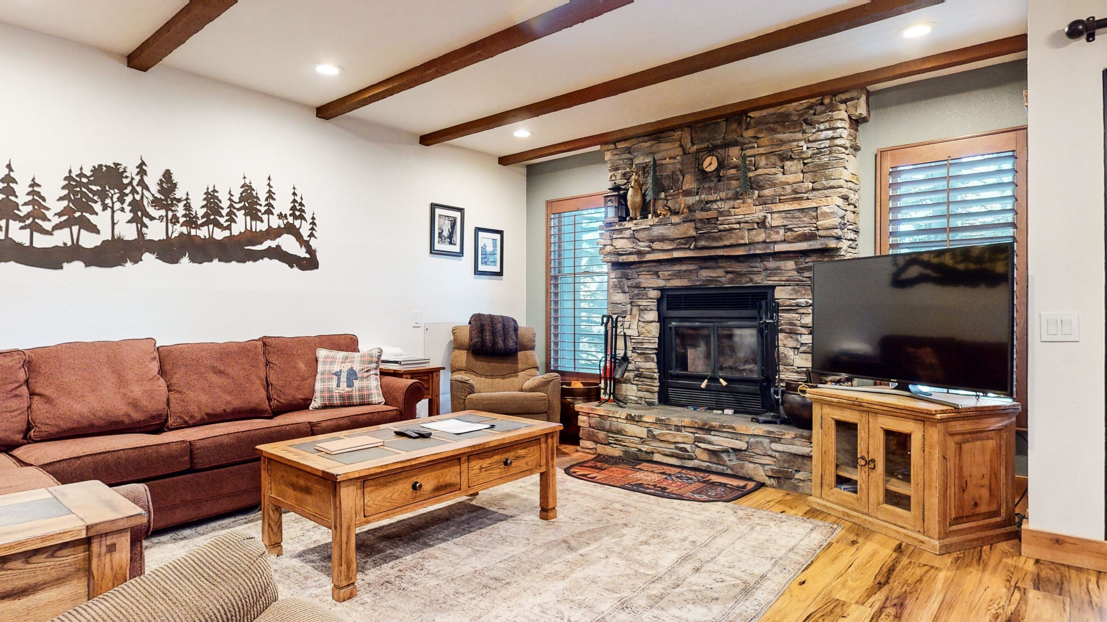 Una sala de estar acogedora con chimenea de piedra, un televisor de pantalla plana grande, un sofá de cuero marrón y una mesa de centro de madera.