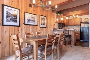 A wooden-paneled dining area with a table and chairs, framed pictures on the wall, and a kitchen with wooden cabinets and appliances. - Val DIsere 32 Pet-Friendly, Walk To The Village, Private Washer Dryer, Spacious Floorplan by RedAwning (Mammoth Lakes)