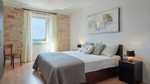 A bedroom with a bed, a nightstand, a chair, a window with curtains, and a wall-mounted abstract painting. - Nice family house for 2 to 4 people (Ližnjan)
