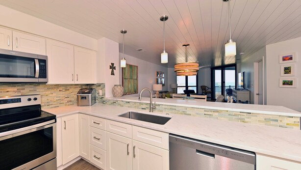 Una cocina moderna con armarios blancos, electrodomésticos de acero inoxidable, una isla grande con un fregadero e iluminación colgante.