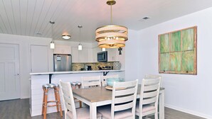 Una cocina moderna con armarios blancos, un refrigerador de acero inoxidable y una mesa de comedor de madera con cuatro sillas.