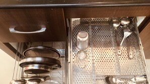 Une cuisine équipée d’ustensiles de cuisine et de casseroles en acier inoxydable, rangés de manière ordonnée sur un plateau perforé.