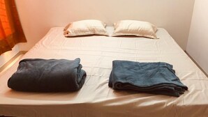 Un lit simple avec un matelas blanc et deux oreillers, une couverture bleu foncé pliée sur la gauche et une serviette bleu foncé pliée sur la droite.