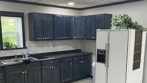 A modern kitchen with dark cabinets, a white refrigerator, and a window with a view of greenery. - Working farmette at converted warehouse in the Allegany Mountains. (Allegany)