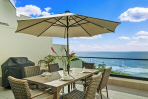 Un espace repas avec une table, des chaises et un parasol, donnant sur l’océan.