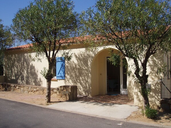 A building with a tiled roof, an arched doorway, and a small tree in front.