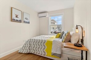 A bedroom with a bed, bedside table, lamp, and two framed pictures on the wall.