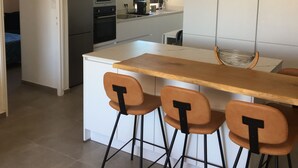 A modern kitchen with a central island, four bar stools, a microwave, and a sink. - Superb apartment with sea and mountain views (Canet-en-Roussillon)