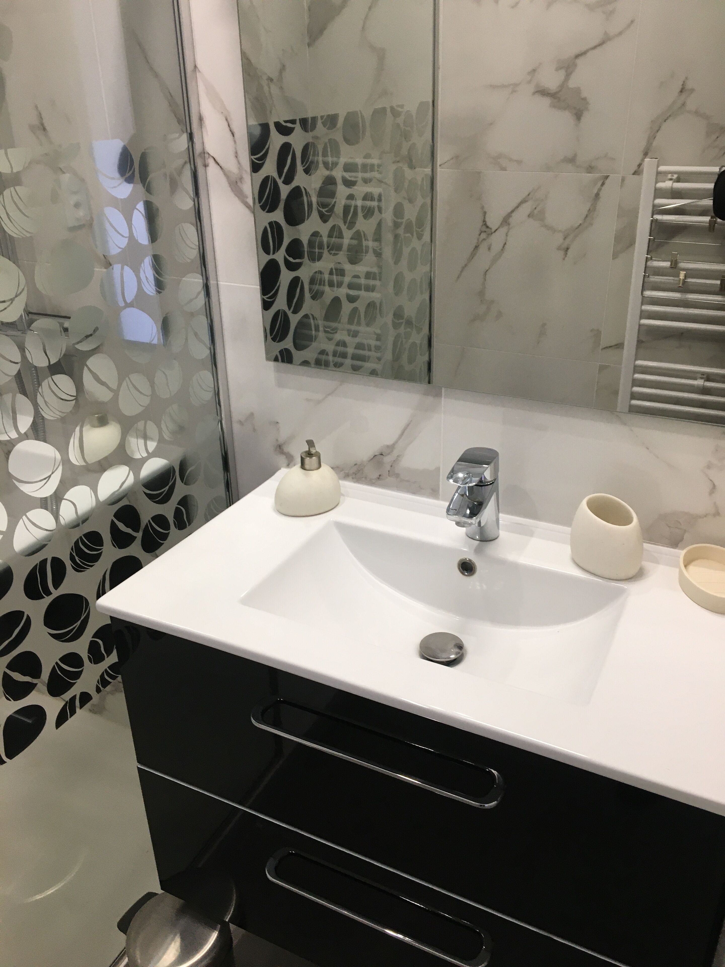 A bathroom with a white sink, two white soap dispensers, a mirror, and a towel rack.