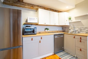 Una cocina moderna con armarios blancos, un refrigerador de acero inoxidable, un microondas, un tostador y un lavavajillas.