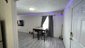 Ett rum med ett matbord, stolar, en tv som är monterad på väggen och en taklampa.