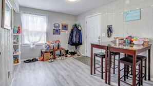 Ett rum med trägolv, ett matbord med stolar, en klädhängare och ett fönster med gardiner.