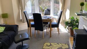 A modern living room with a black sofa, a dining table with chairs, a coffee table, and a large window with curtains. - Homely 2- bed Apartment -ground Floor-sleeps 4 (Ilfracombe)