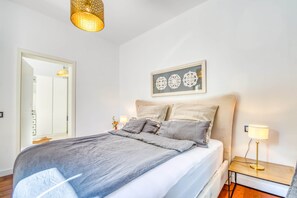 A bedroom with a bed, bedside tables, a hanging light fixture, a framed artwork, and a mirror.