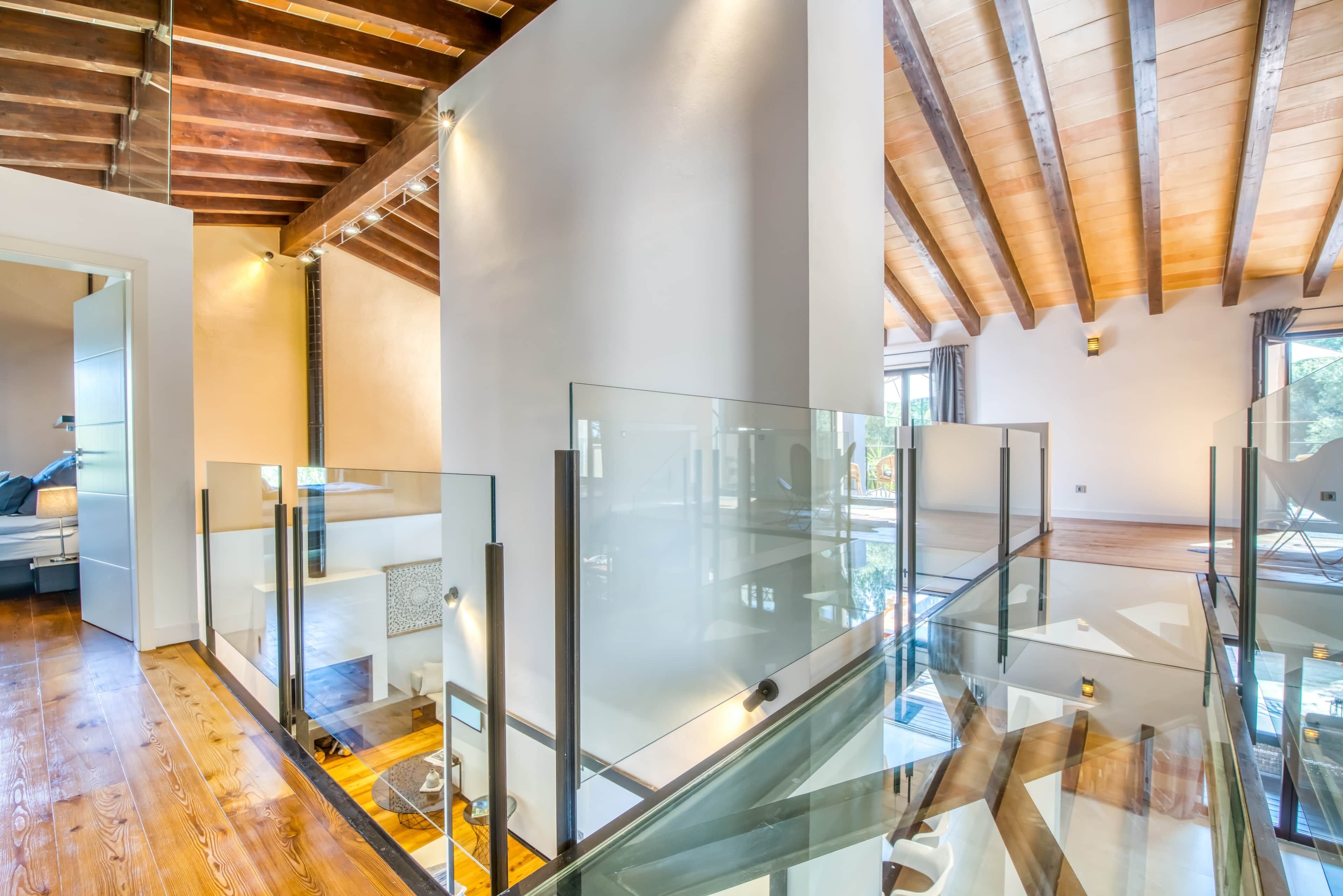 A modern interior with a glass staircase, wooden floors, and exposed beams.