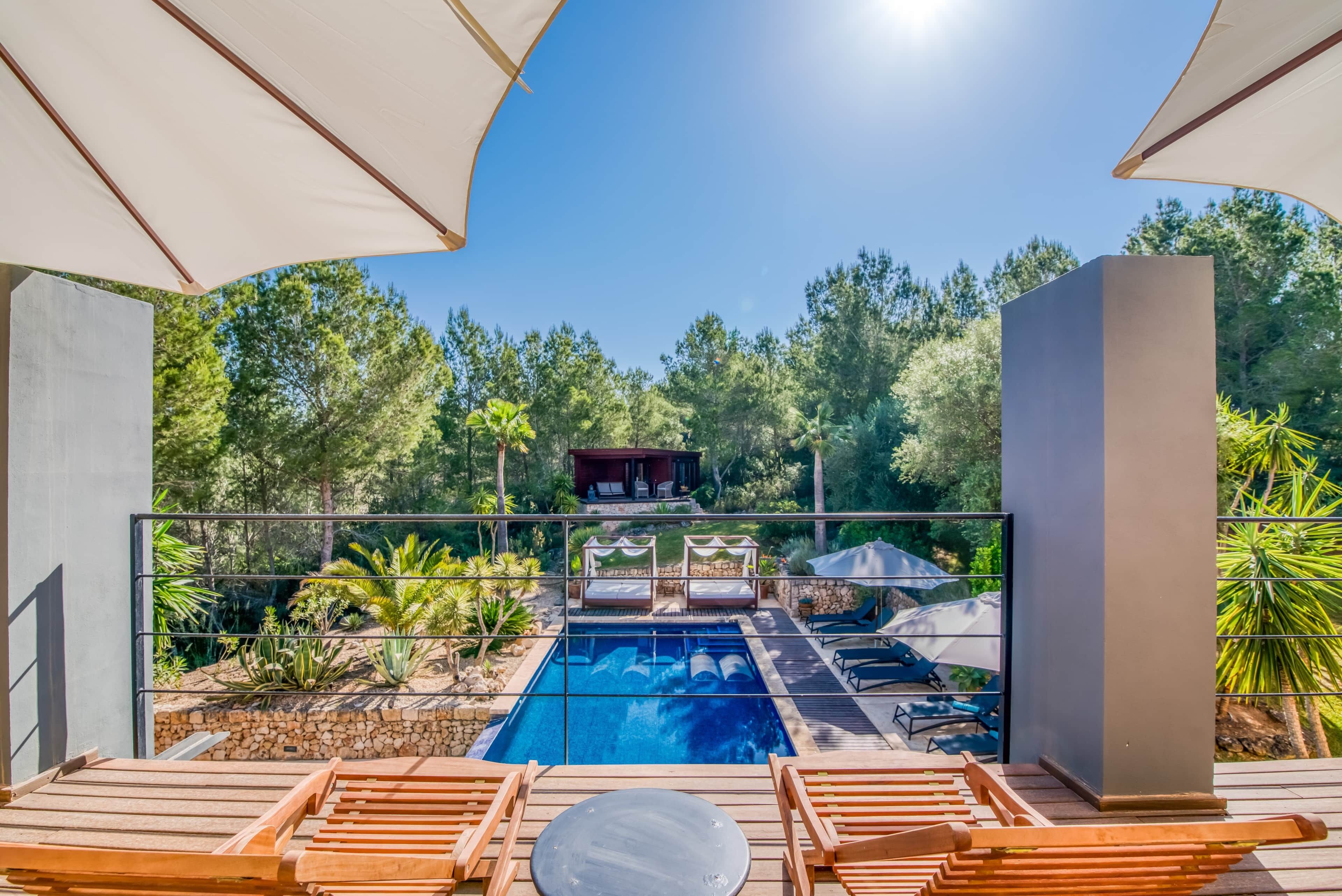 A pool area with lounge chairs, a stone wall, and a view of the surrounding greenery.