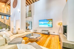 Uma sala de estar moderna com uma grande televisão de tela plana, uma mesa de centro de vidro e piso de madeira.